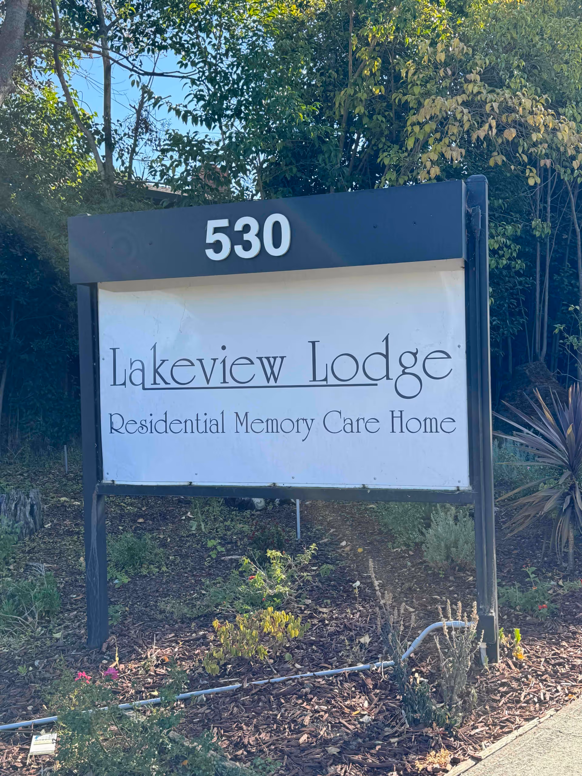 Outdoor sign reading "530" and "Lakeview Lodge Residential Memory Care Home" set in a landscaped area with trees and shrubs behind it.
