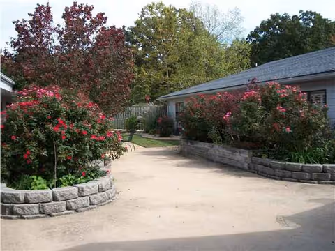 A curved walkway flanked by stone planters with pink roses leads to a single-story building exterior.