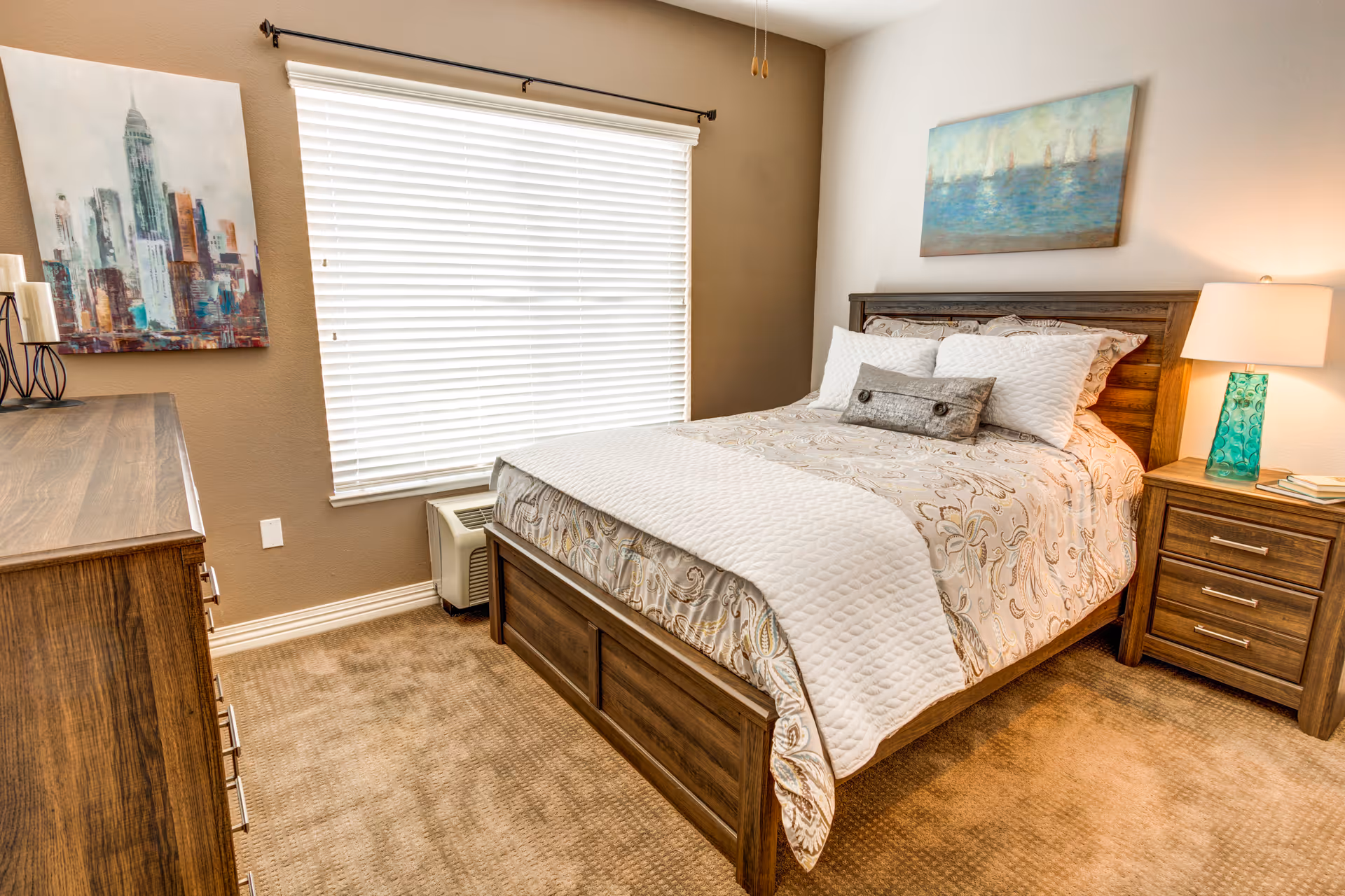 A furnished bedroom with a wooden bed and matching nightstand and dresser, carpeted floor, and a window with blinds.