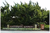 Exterior view of Hacienda Carmel Community entrance with landscaped sign and trees.