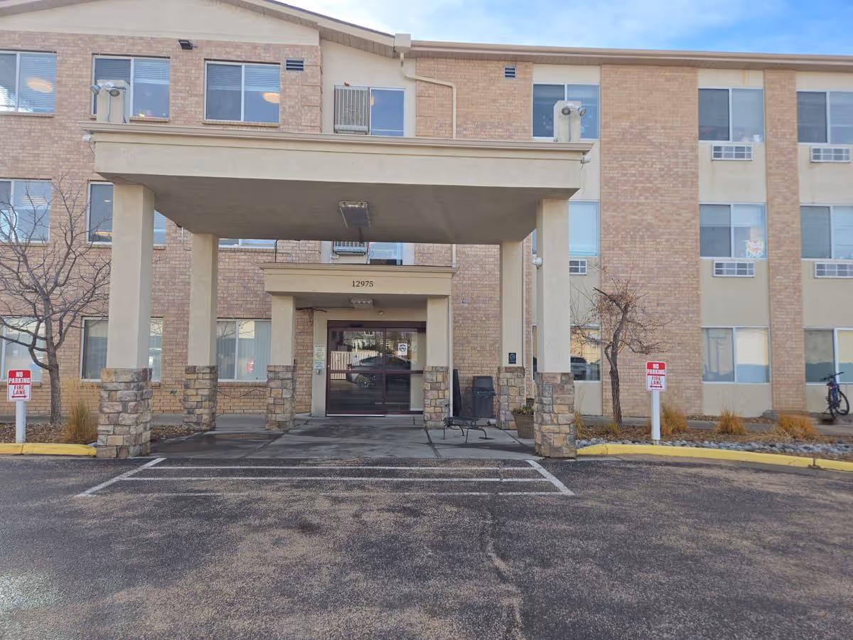 Covered entrance and drop-off canopy of a multi-story brick senior living building with the address '12975' above the doors.