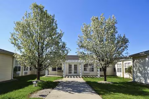 Front exterior of a senior living building with entrance doors and trees.
