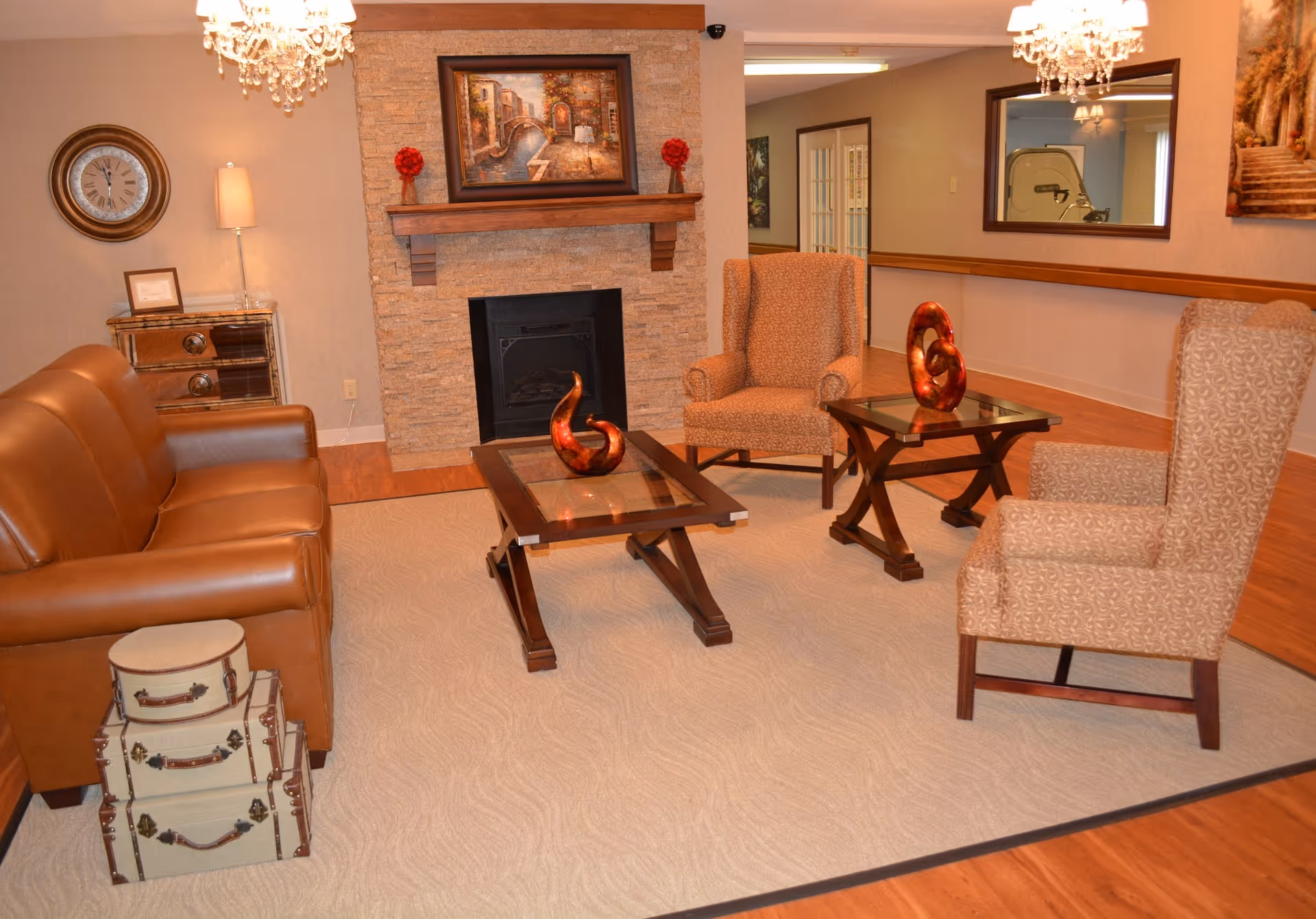 Cozy sitting area with a leather sofa, upholstered armchairs, glass-top coffee tables, decorative sculptures, and a stone fireplace.