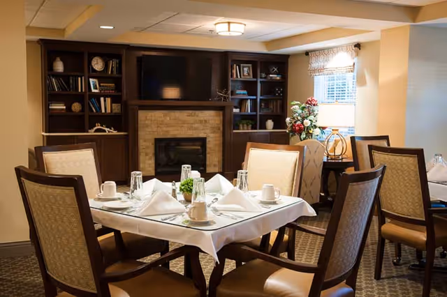 Cozy dining area with a set table, upholstered chairs, and a fireplace flanked by built-in shelves.