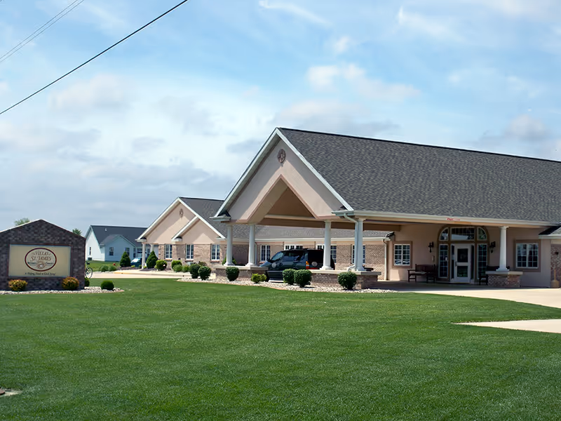 Exterior view of The Villas at St. James facility showing a single-story building with a covered entrance, manicured lawn, and a sign displaying the facility's name.