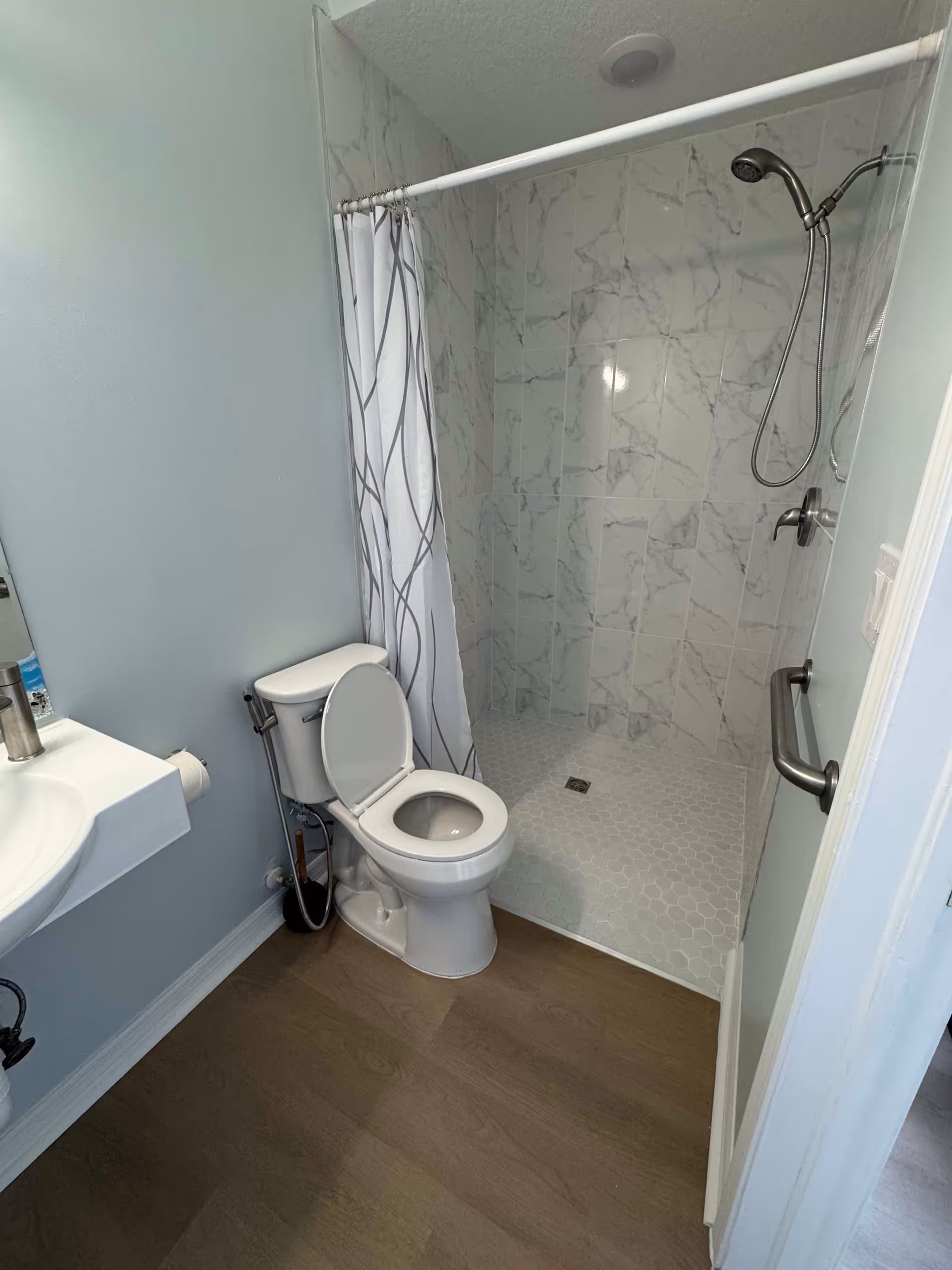 Small bathroom with a toilet, wall-mounted sink and a walk-in tiled shower with a curtain.