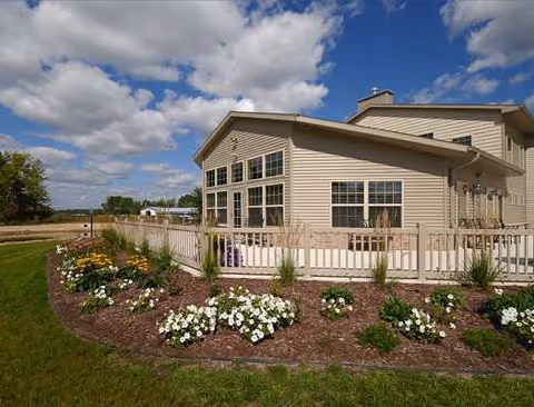 Exterior view of The Cottages on Golden Pond Senior Living with landscaping and a white railing.