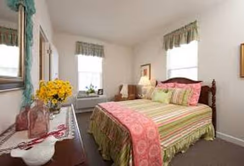 A cozy bedroom in a senior living facility featuring a colorful striped bed and dresser.