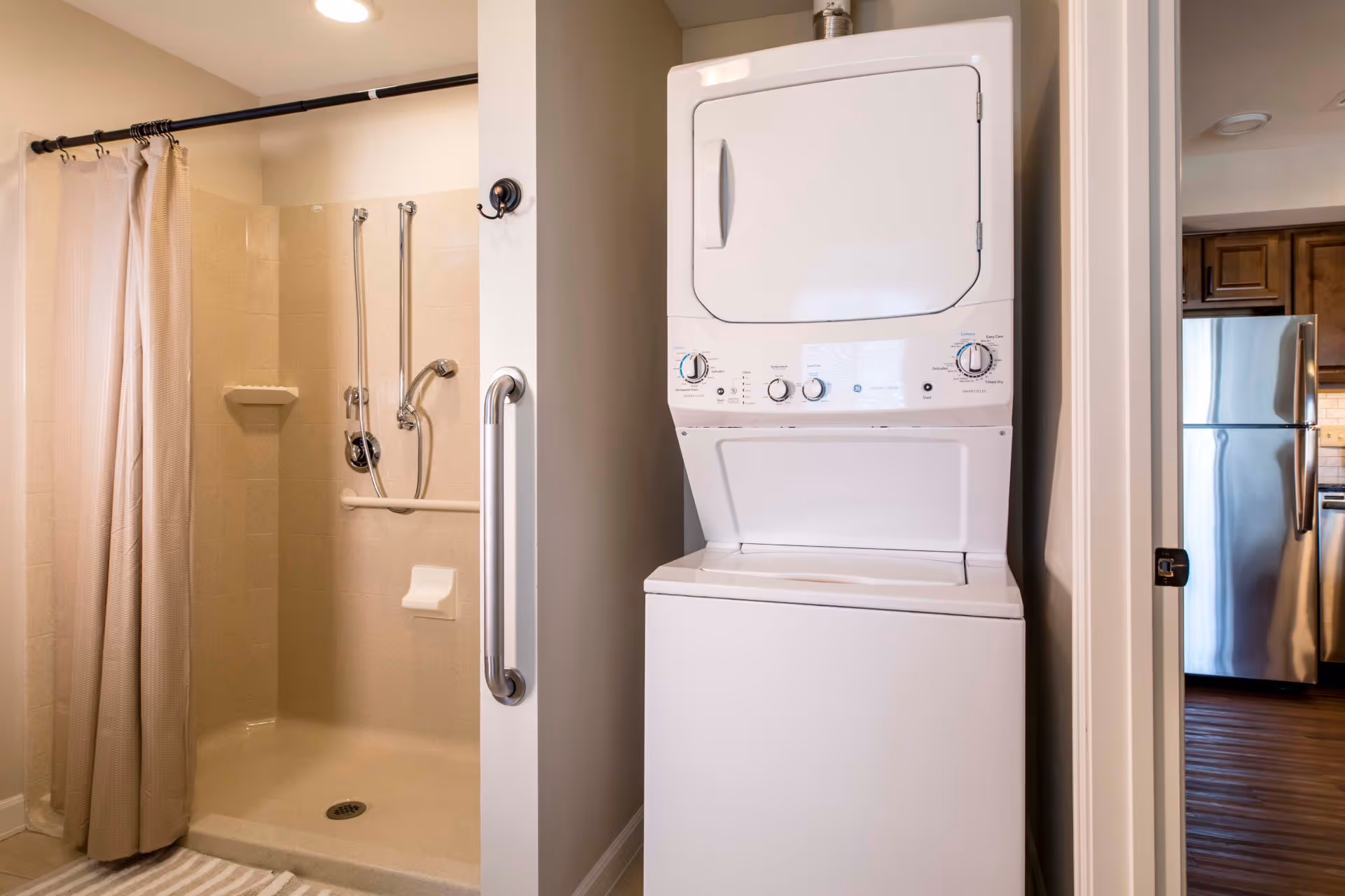 A stacked washer and dryer unit next to an accessible shower with grab bars and a curtain.