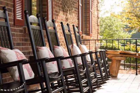 Row of black rocking chairs with cushions on a brick porch outdoors.