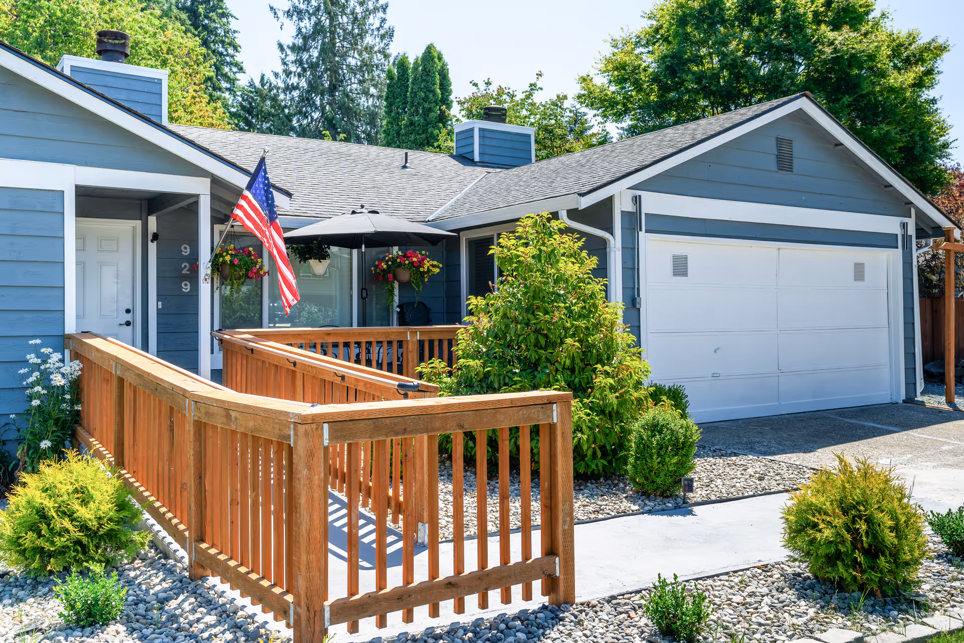 Front exterior of a single-story home with a wooden ramp, American flag, garage, and landscaping.