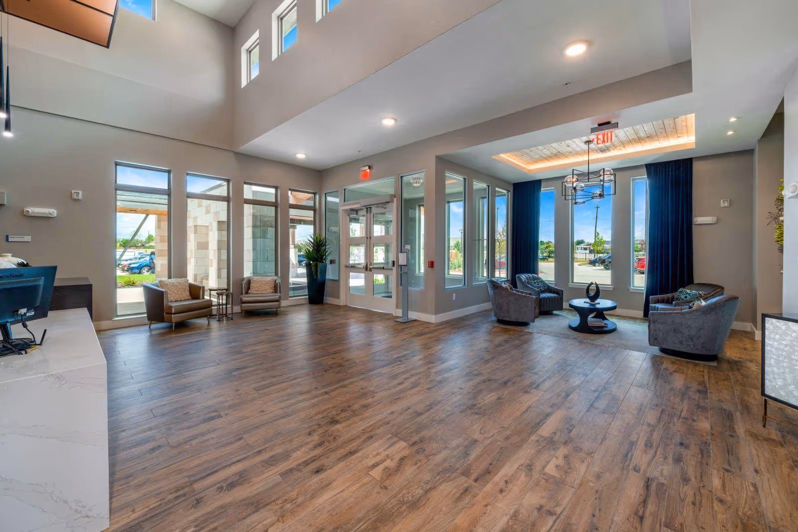 Bright, open lobby with wood flooring, seating areas, a reception desk, and tall windows at the entrance.