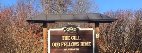 Outdoor sign reads The Gill Odd Fellows Home, with bare trees in the background.