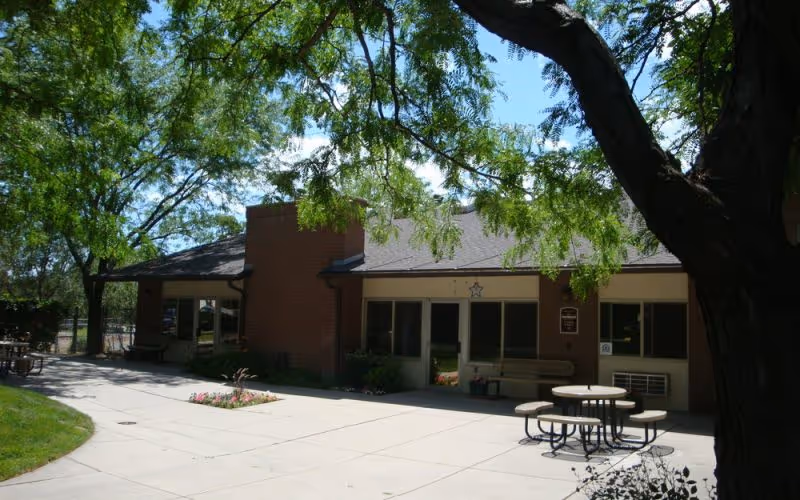Capitol Villa exterior building with shaded courtyard, trees, and round outdoor tables.