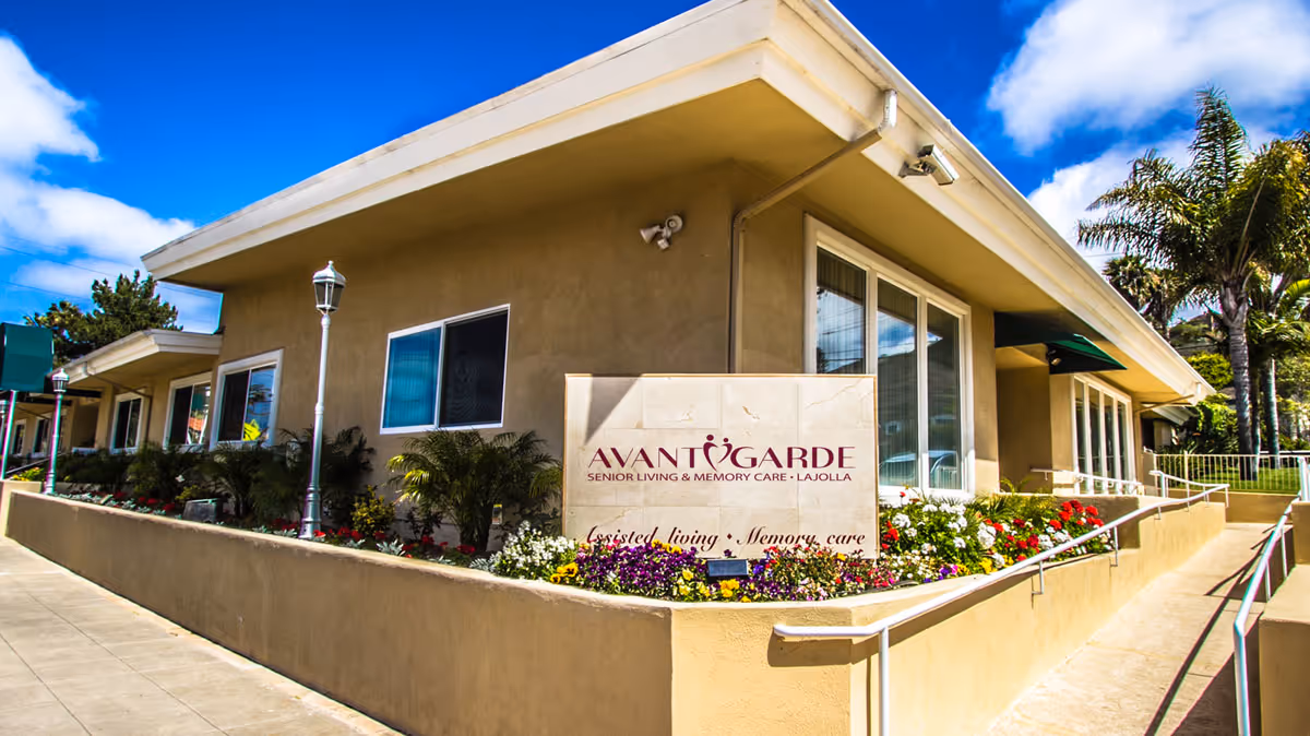Exterior front of the Avantgarde Senior Living building with a sign, flowerbeds, and a ramped walkway.