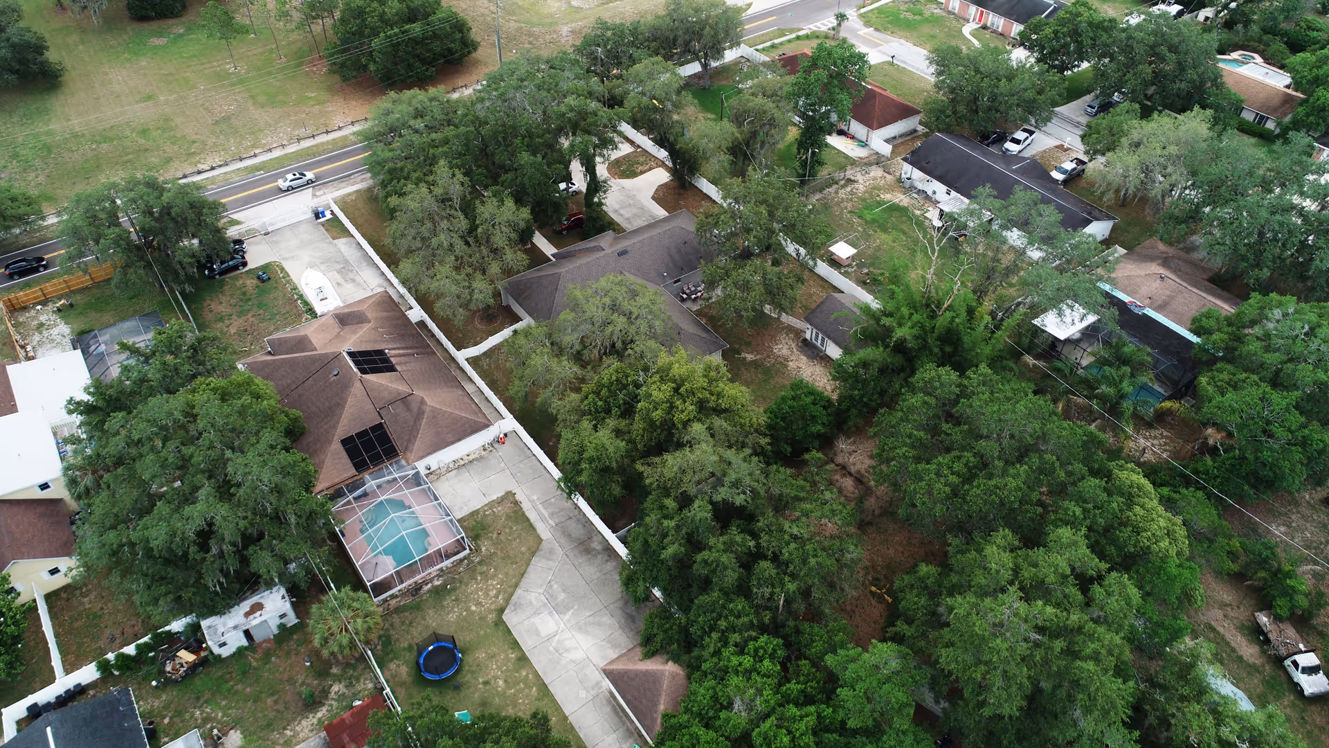 Aerial view of a tree-lined residential property with several houses, driveways, and a screened pool enclosure.