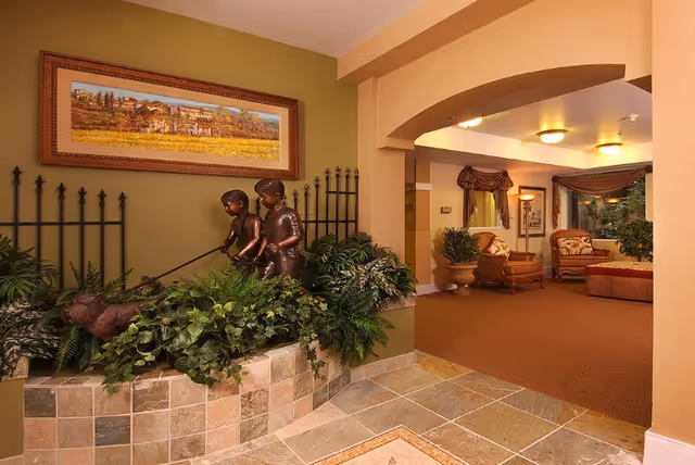 Interior lounge area with a bronze sculpture of two children among plants by a tiled planter and an arched entry to a seated sitting room.
