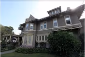 Exterior front view of a two-story Victorian-style residence with bay windows, pitched roofs, and surrounding shrubs and lawn.