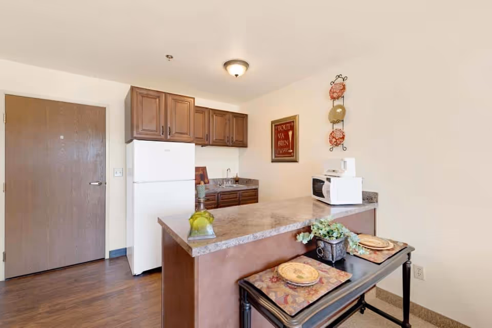 Kitchenette featuring a refrigerator and wooden cabinets, a marble-look countertop island with place settings and a microwave.