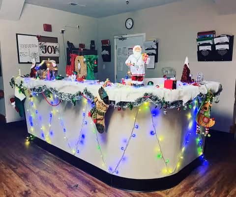 Reception desk decorated with Christmas garlands, string lights, stockings, and a Santa figurine in a senior care facility.