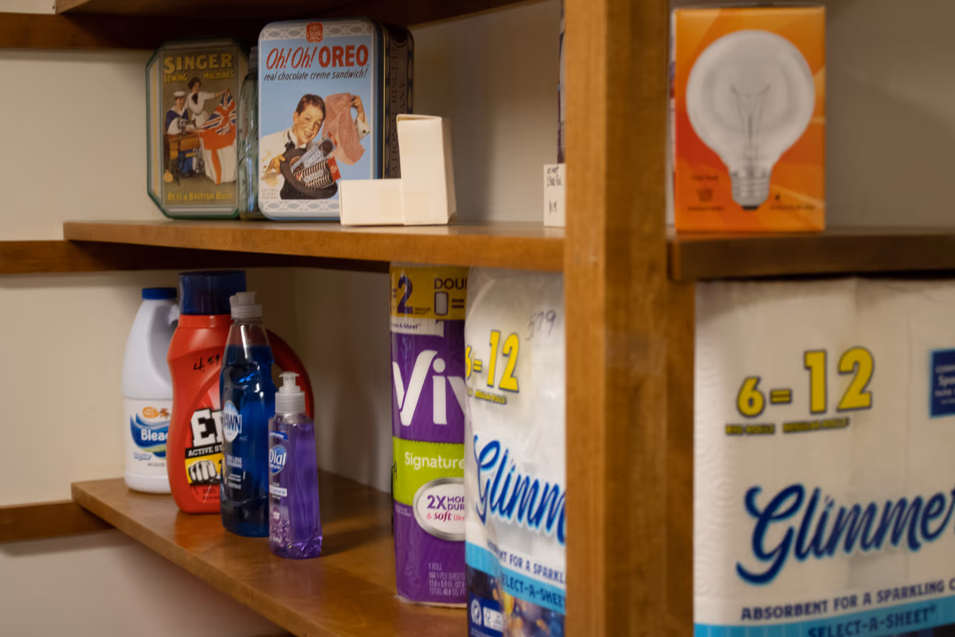 Wooden shelving holding cleaning supplies, paper towels and decorative tins.