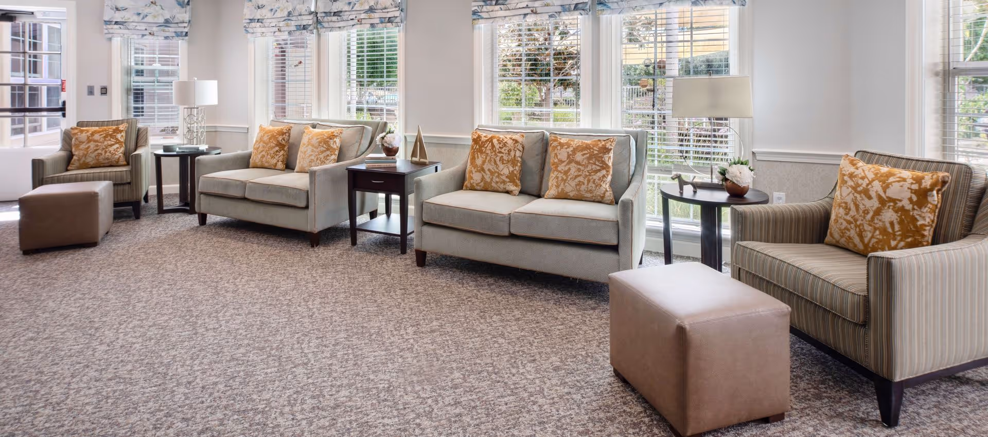 Bright common lounge with sofas, armchairs, ottomans and side tables arranged in front of large windows.