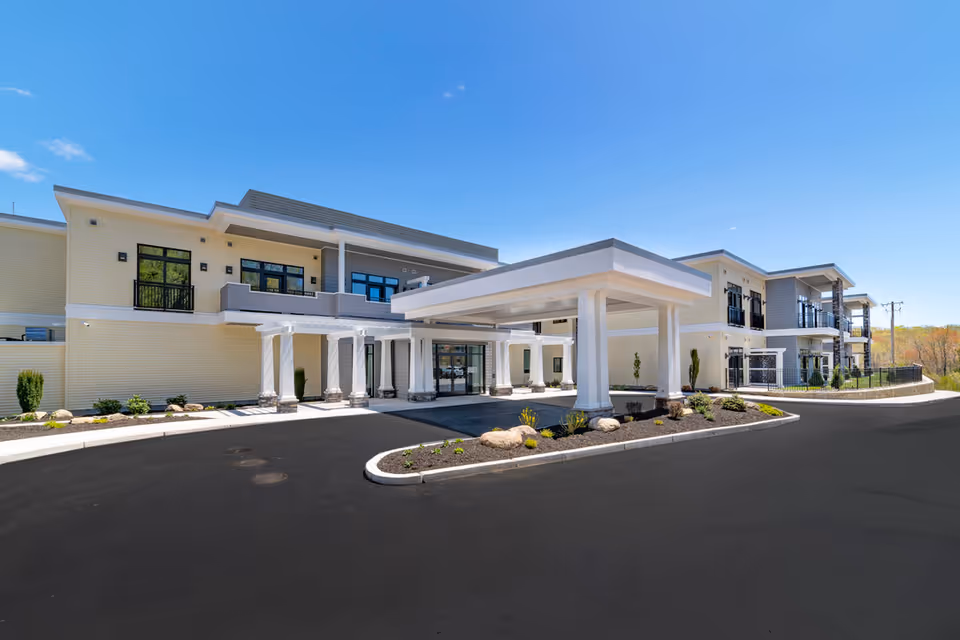 Exterior view of Briarcliffe Preserve Assisted and Independent Living facility showing a modern two-story building with a covered entrance, columns, balconies, and landscaped areas under a clear blue sky.