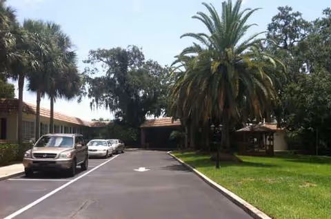 Entrance drive with parked cars, palm trees, and buildings at Grace Rehabilitation Center of Vero Beach.
