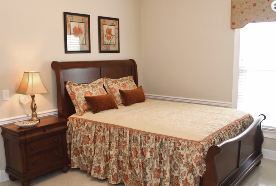 A warmly decorated bedroom with a wooden sleigh bed dressed in floral bedding, a nightstand with lamp, and framed artwork on the wall.