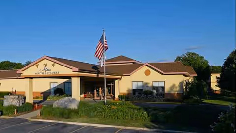 Front exterior of a single-story senior living building with a flagpole and landscaping.
