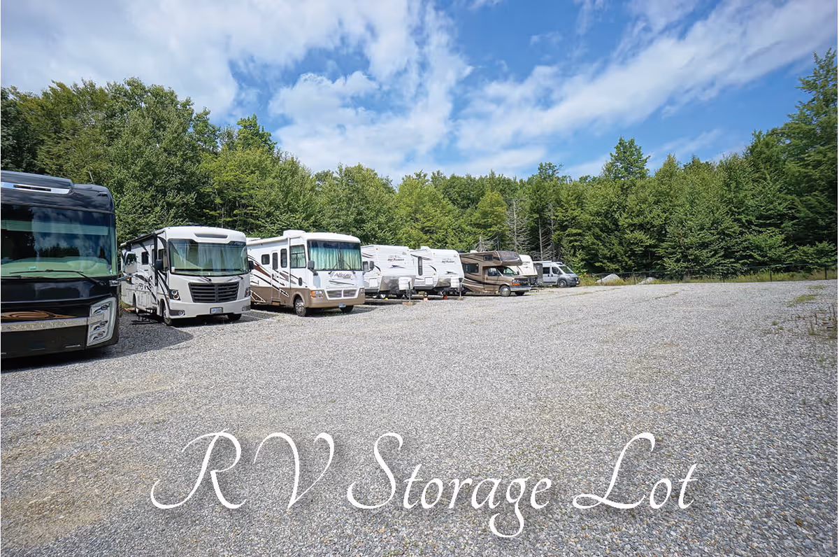 A gravel lot with several recreational vehicles (RVs) parked in a row along the left side, surrounded by dense green trees under a partly cloudy blue sky. Text on the image reads 'RV Storage Lot'.