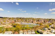 Aerial view of a suburban neighborhood with numerous houses, a large sports field with a running track, and a clear blue sky with scattered clouds.