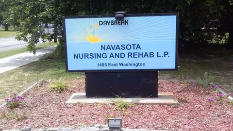 A Daybreak sign reading Navasota Nursing and Rehab L.P. on a landscaped front lawn.
