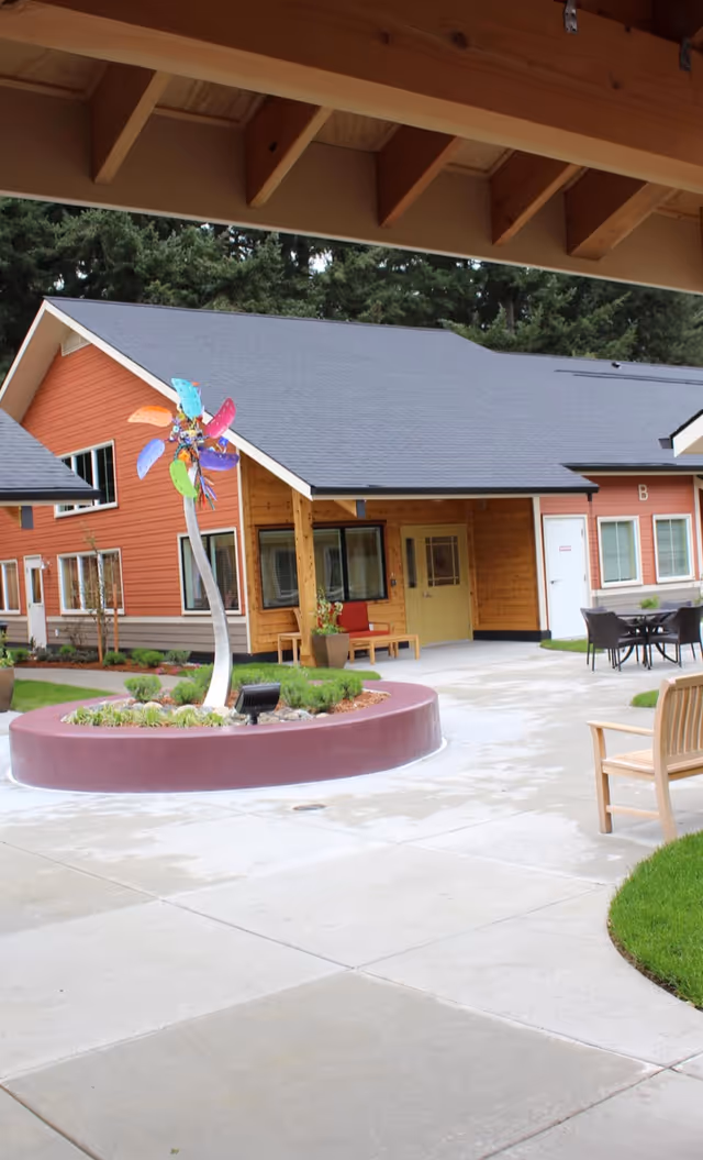 Courtyard of a cottage-style senior living building with a colorful wind sculpture, circular planter, benches and outdoor seating.