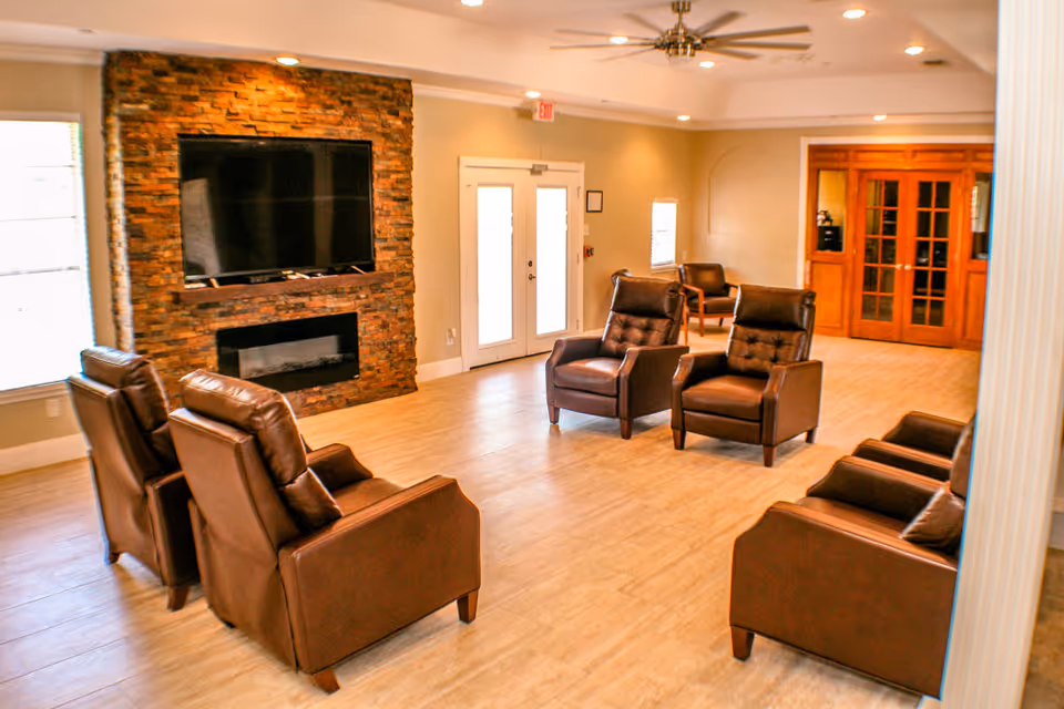 Community lounge with brown leather armchairs arranged around a wall-mounted TV above a stone fireplace.