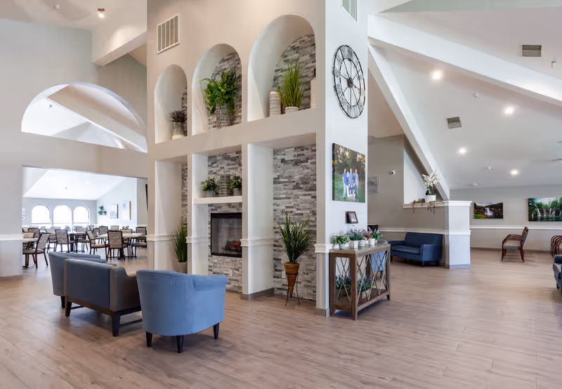 Spacious senior living lobby with arched alcoves, fireplace, and comfortable seating.