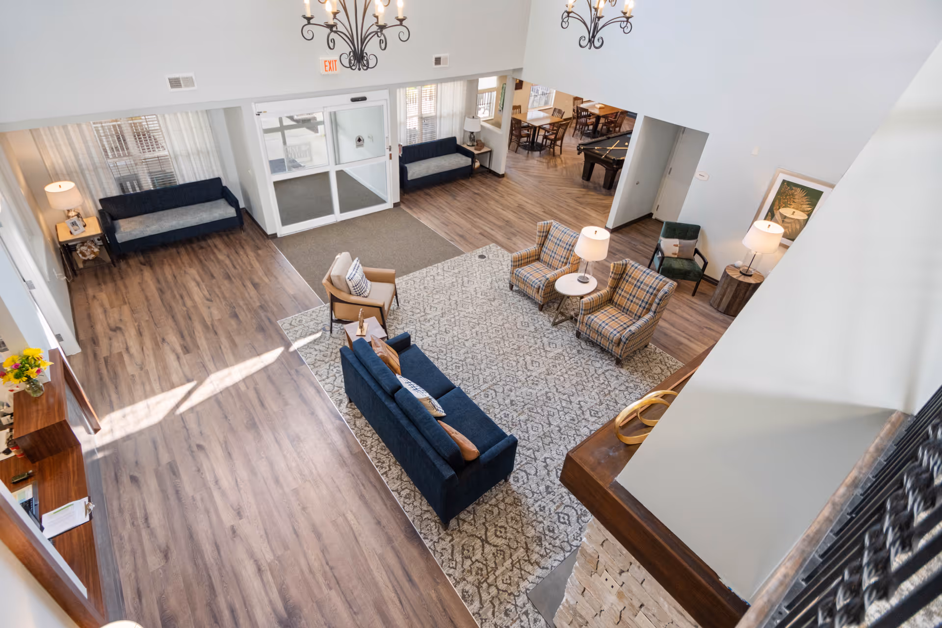 Bright open lobby with sofas, armchairs, rug and entry doors viewed from an upper level.
