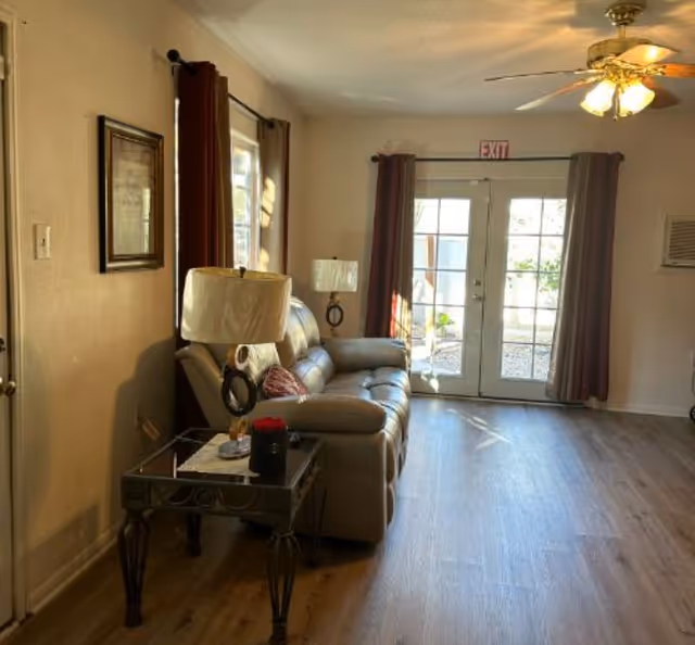 Cozy living room with a leather sofa, side table, lamps, and French doors to outdoor area.