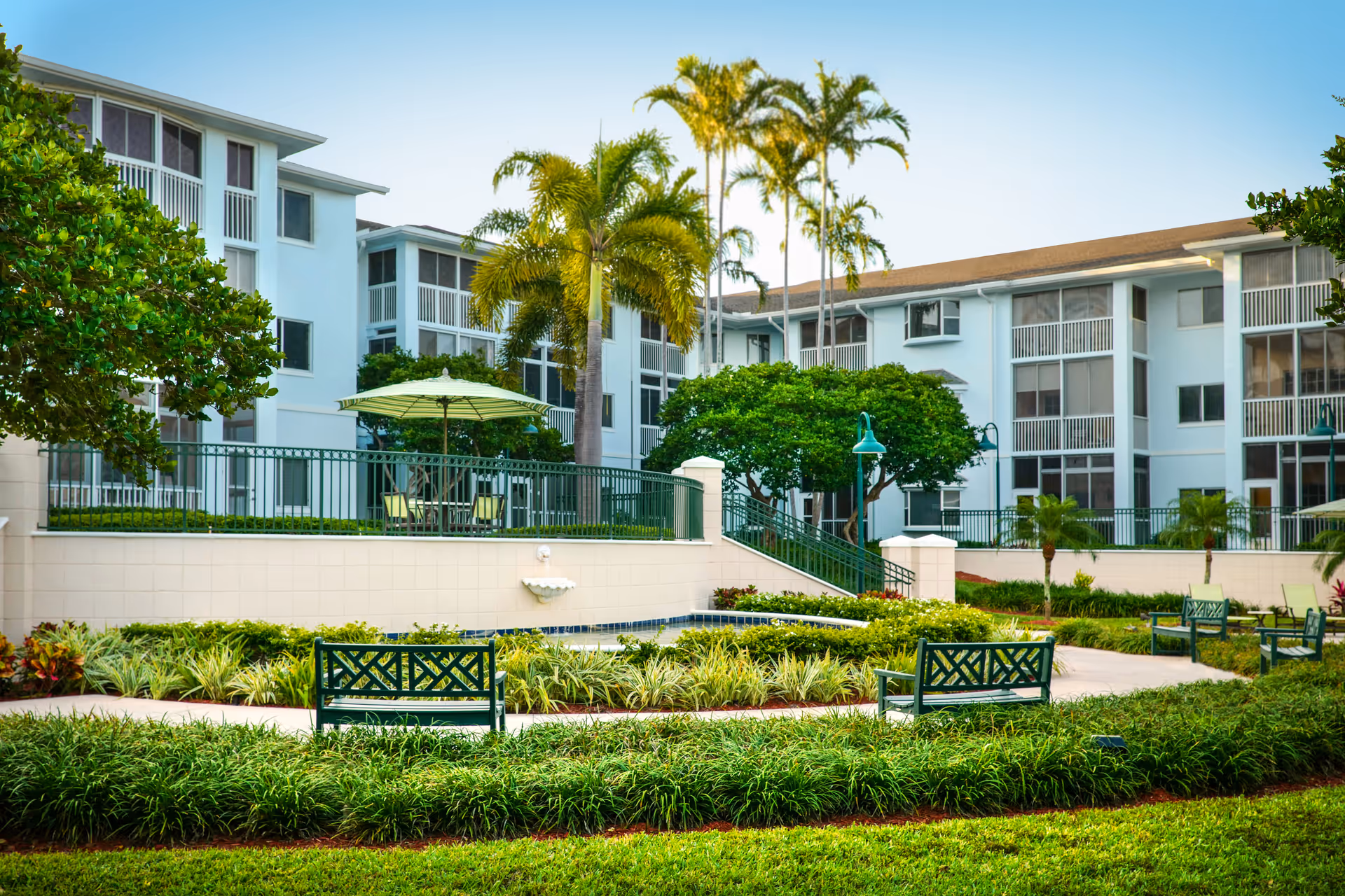 Landscaped courtyard with benches, walkways, palm trees, and a multi-story residential building in the background.