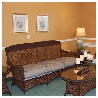 Wicker sofa with patterned cushions, matching coffee table topped with candles, a table lamp, and framed artwork in a cozy sitting area.