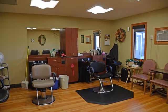 Interior salon room with barber chairs, mirrors, cabinetry, and a few waiting chairs.