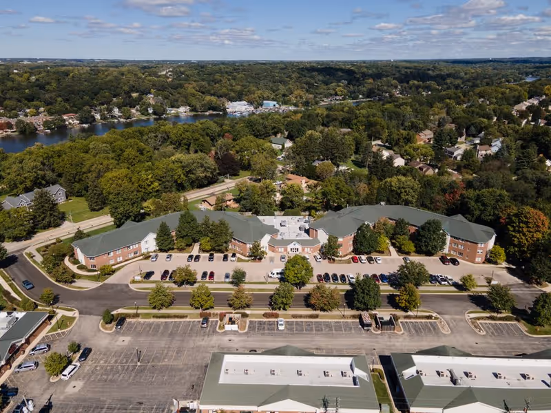 Aerial view of The Pointe at Eastgate senior living complex with parking lots, surrounded by trees and a river in the background.