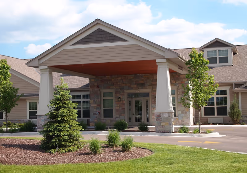 Exterior view of Sunrise Meadows Senior Living entrance with stone pillars and porte-cochère.