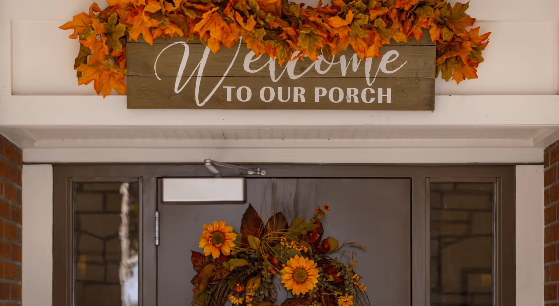 Entrance door decorated with a fall wreath and a wooden sign reading "Welcome to Our Porch" above it.