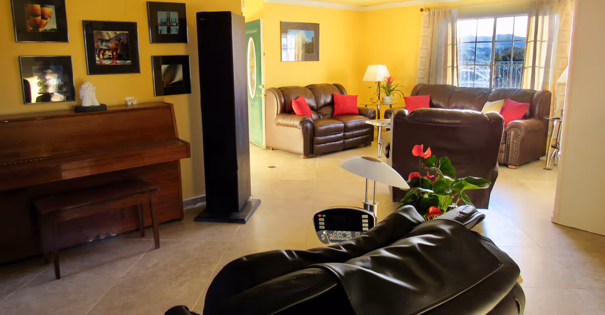 Bright living room with yellow walls, leather sofas and chairs, a piano, a recliner, and a large window.