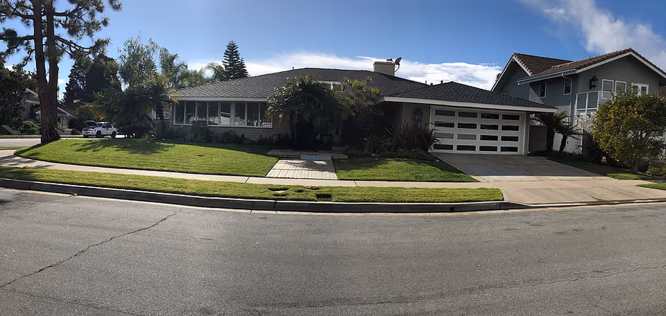 Front exterior of a single-story suburban house with a manicured lawn, driveway and attached garage under a blue sky.