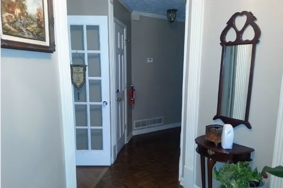 A home's entry hallway with a glass-paned door, small wooden console table and mirror, and framed wall art.