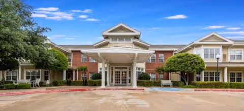 Front view of Wyndham Court of Plano entrance with porte-cochère and greenery.