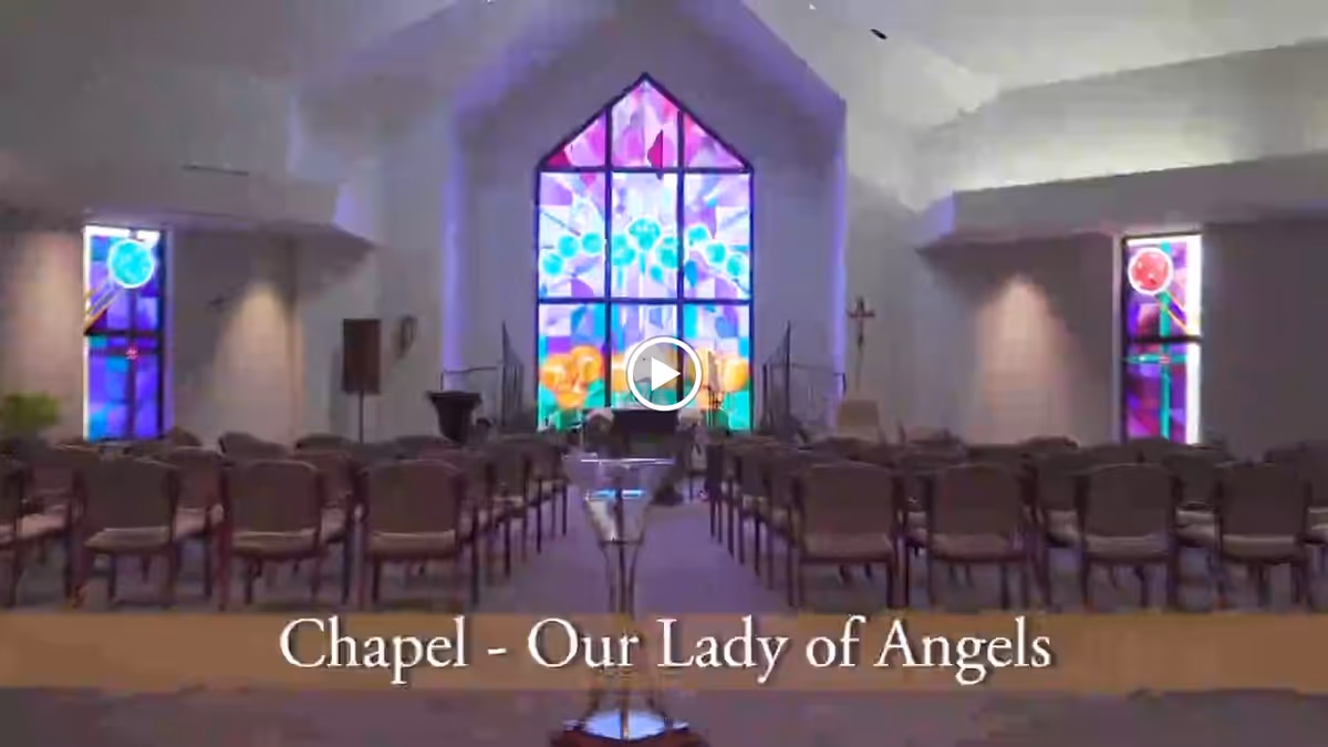 Interior of a chapel with rows of chairs facing a large colorful stained-glass window.