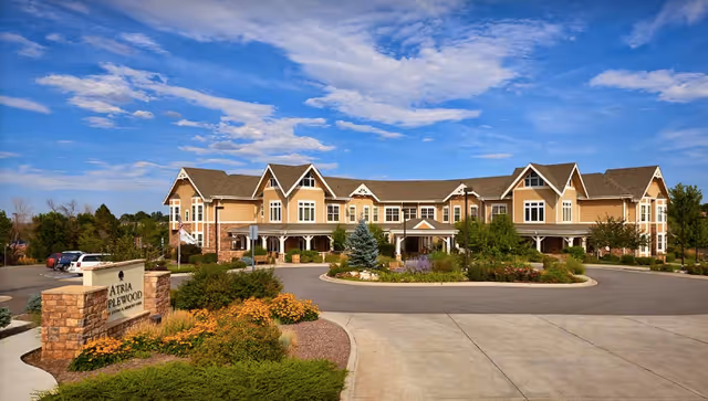 Wide view of a large two-story assisted living building with pitched roofs, landscaped grounds and a circular driveway with an entrance sign.
